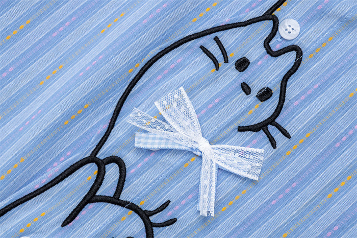 Close-up of a cat embroidery with a textured white bow on the light blue striped shirt