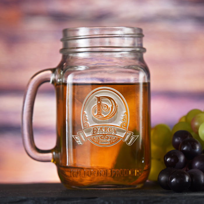 Mason jar mug with a handle, sand-carved with an initial in an oval crest above a name banner.