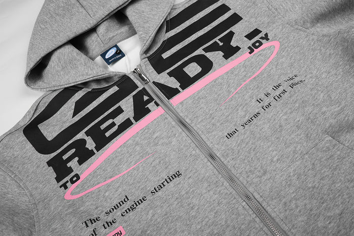Detailed view of gray hoodie front graphic with READY lettering, pink oval line, zipper, and printed text