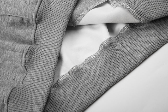 Close-up of gray hoodie ribbed hem and seam with the light-colored inner lining visible