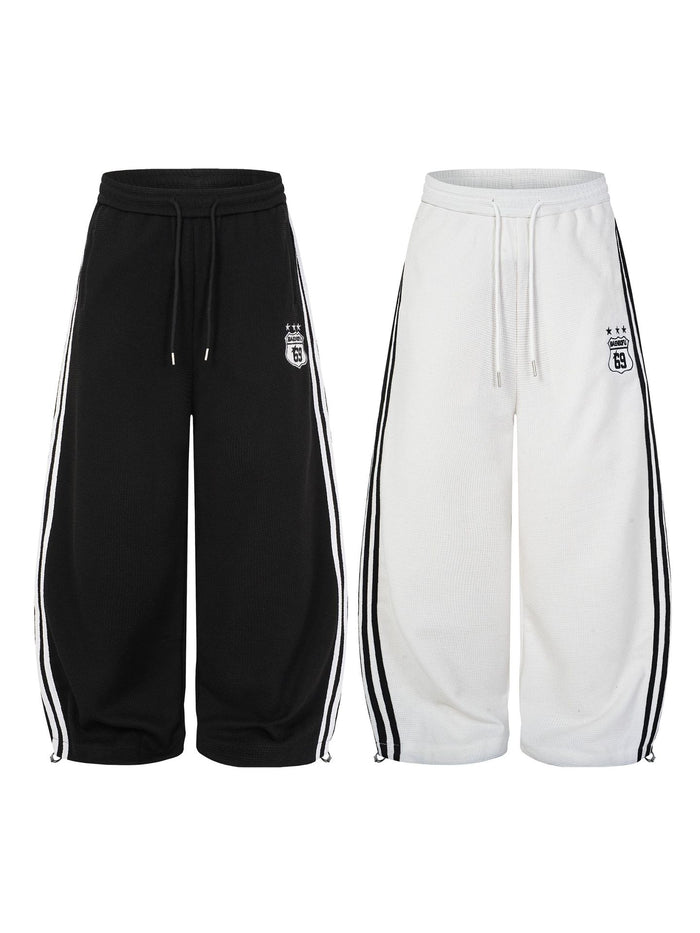 Black and white wide-leg track pants with contrasting side stripes and embroidered shield badges