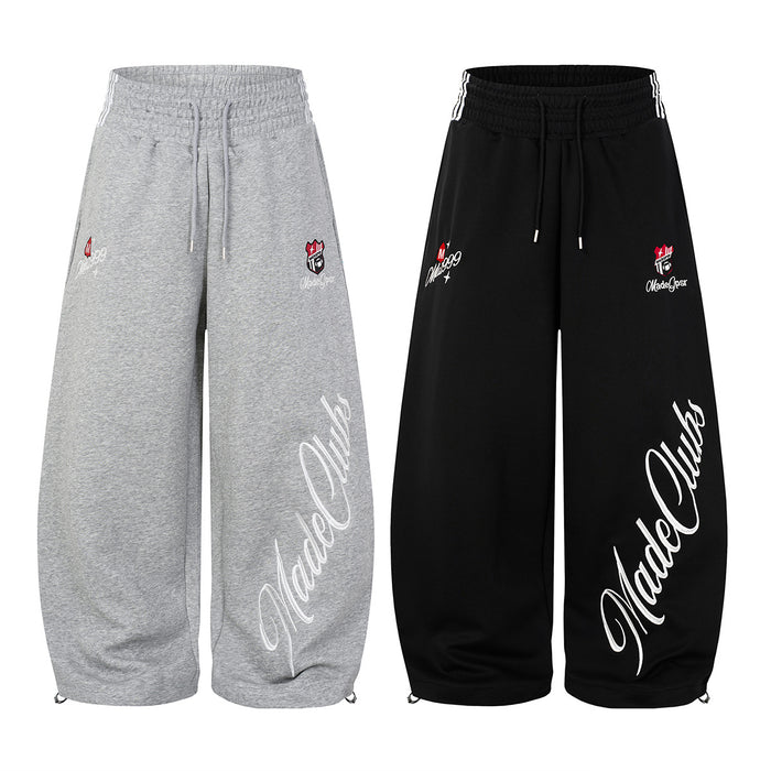 Front view of gray and black wide-leg sweatpants with drawstrings, embroidered badges, and large white script