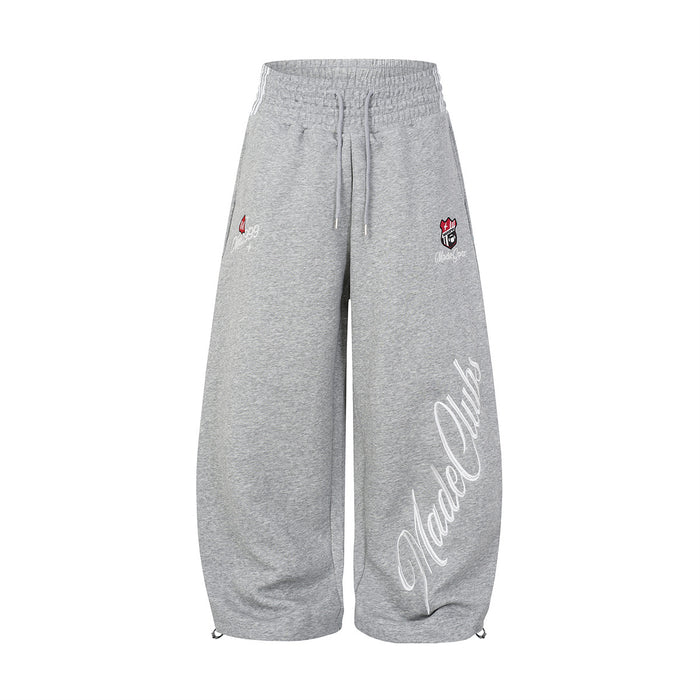Front view of gray wide-leg sweatpants with drawstring waist, chest-style badges, and large white script