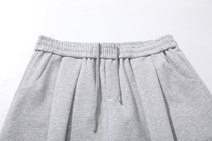 Close-up of light gray sweatpants waist with elastic band, drawstring, and pleated front