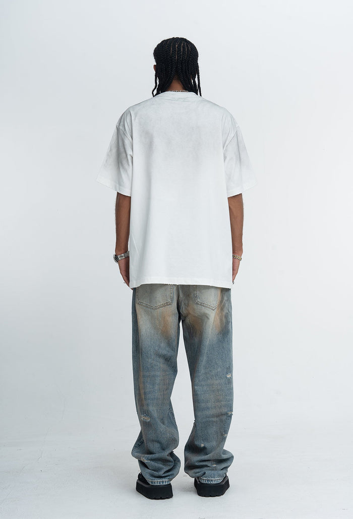Back view of oversized white graphic T-shirt paired with faded wide-leg jeans and black shoes on a studio model