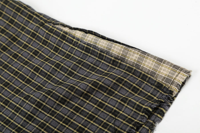 Close-up of black and yellow plaid fabric with distressed raw edges and faded gradient detail