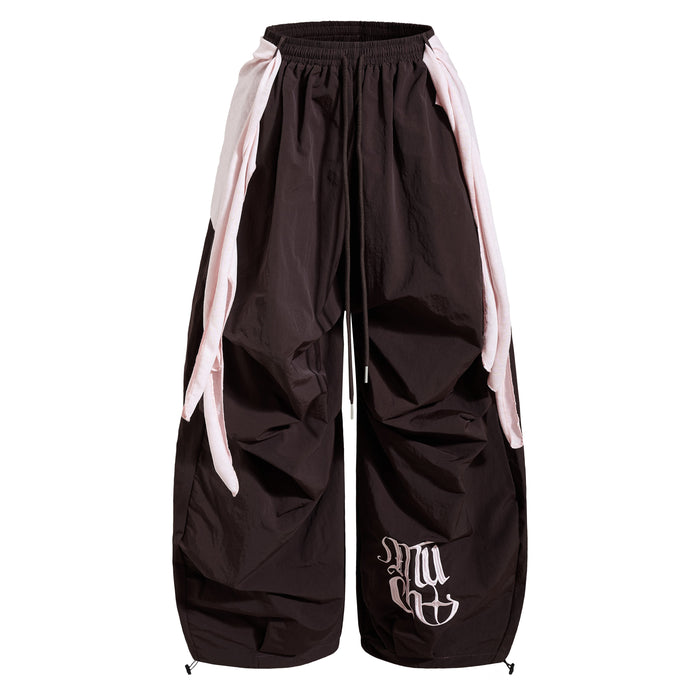 Front view of dark wide-leg nylon pants with pale layered side panels and white graphic
