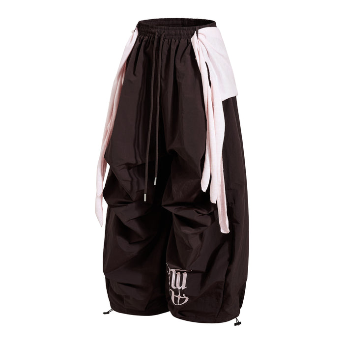 Angled front view of dark wide-leg nylon pants with pale layered side panels and drawstring waist