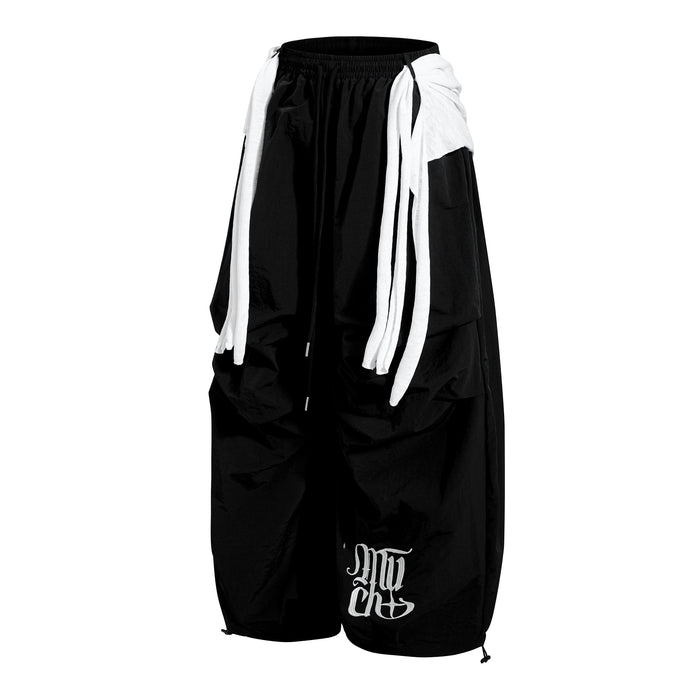 Angled front view of black wide-leg nylon pants with white layered side panels and graphic leg print