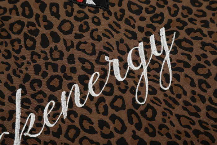 Close-up of brown leopard print polo tee with white script embroidery on textured fabric