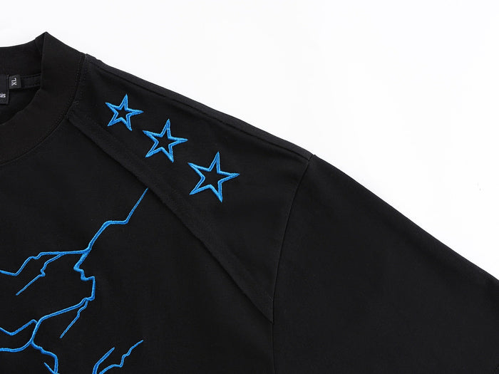 Black oversized graphic tee with blue embroidered lightning bolt and star accents on the shoulder