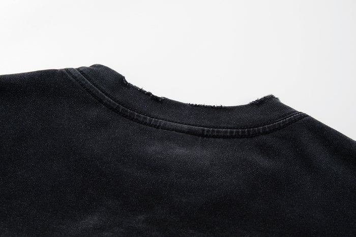 Close-up of a washed black graphic tee collar with frayed edge and vintage worn texture
