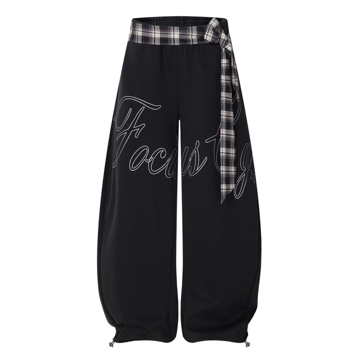 Black barrel track pants with bold script print and plaid tie waist, front view
