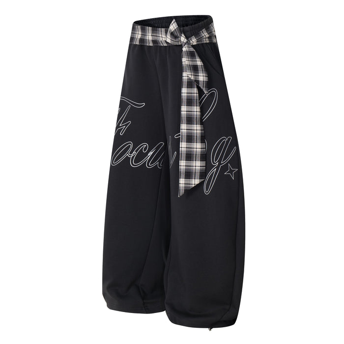 Black barrel track pants with plaid waist tie and script print, angled front view