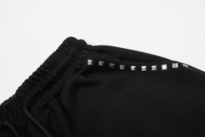 Close-up of silver square studs along the waistband edge of black sweatpants