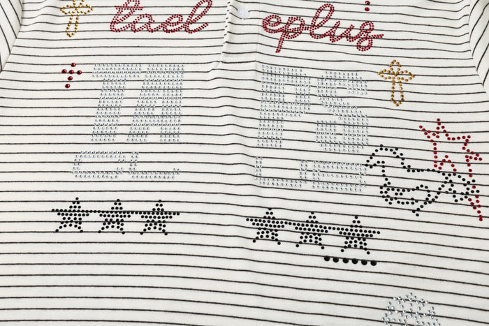 Close-up of cream striped polo chest with red and gold rhinestone script, outlined motifs, and graphic lettering