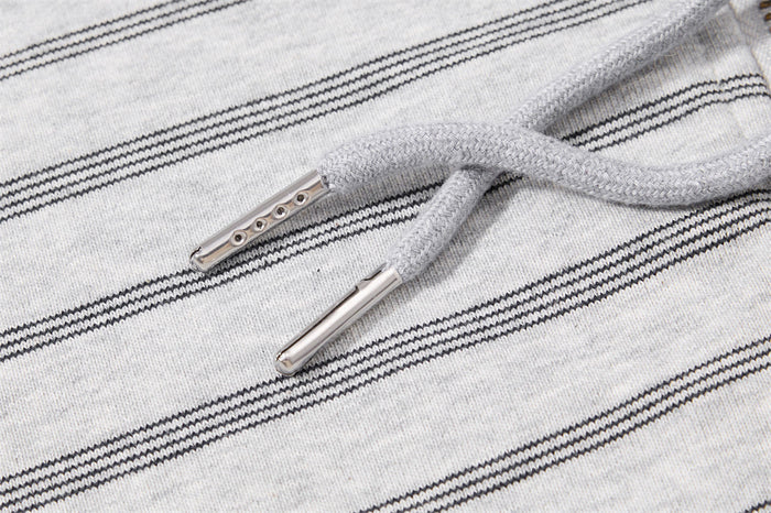 Close-up of gray hoodie drawstrings with metallic aglets against striped fabric