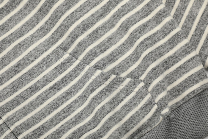 Close-up of a gray and cream striped hoodie front pocket seam beside the ribbed lower hem