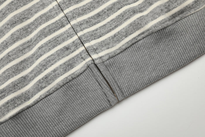 Close-up of the striped hoodie lower edge showing the gray ribbed hem and front zipper seam