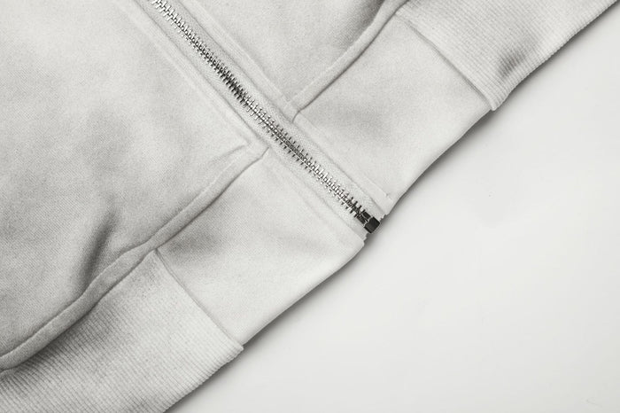 Close-up of the gray hoodie’s front zipper, seam, and ribbed bottom hem