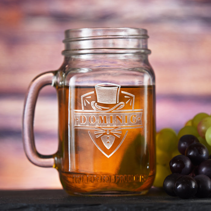 Mason jar mug with a handle, sand-carved with a top hat above a name and bow tie on a shield.
