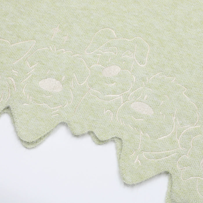 Close-up of pale green knit fabric with outlined puppy illustrations and a wavy scalloped hem