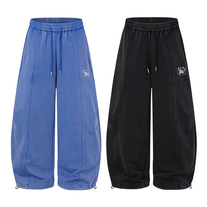 Blue and black wide-leg sweatpants shown from the front with elastic waists, drawstrings, stitched panels, and graphic emblems