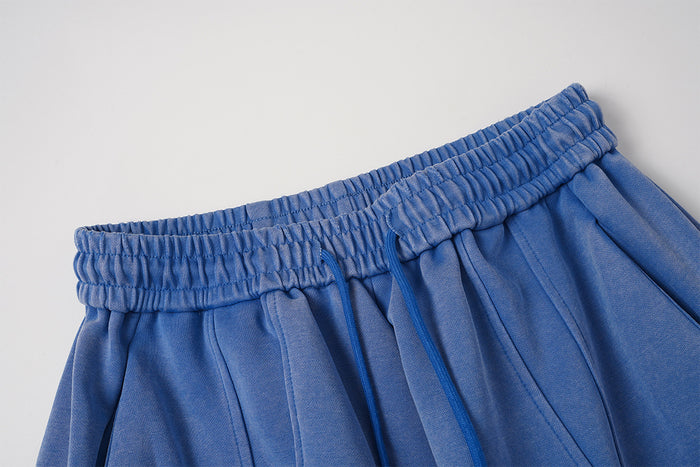 Close-up of the blue sweatpants showing the gathered elastic waistband and vertical stitched leg panels