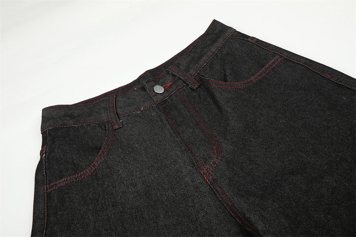 Close-up of black jeans waistband and front pocket with red topstitching and silver button