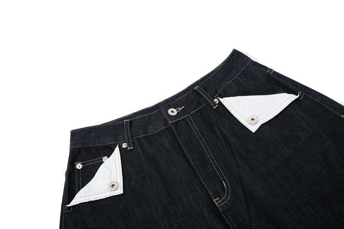 Close-up of the waistband on dark wash denim pants with white contrast pocket flaps and topstitching
