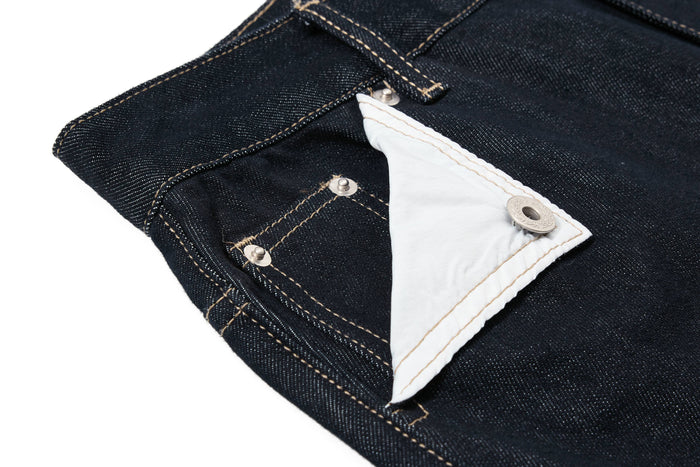 Close-up of a white contrast pocket flap on dark wash denim pants with metal snap hardware