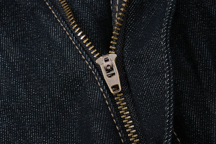 Close-up of the front zipper on dark wash denim pants with tan stitching