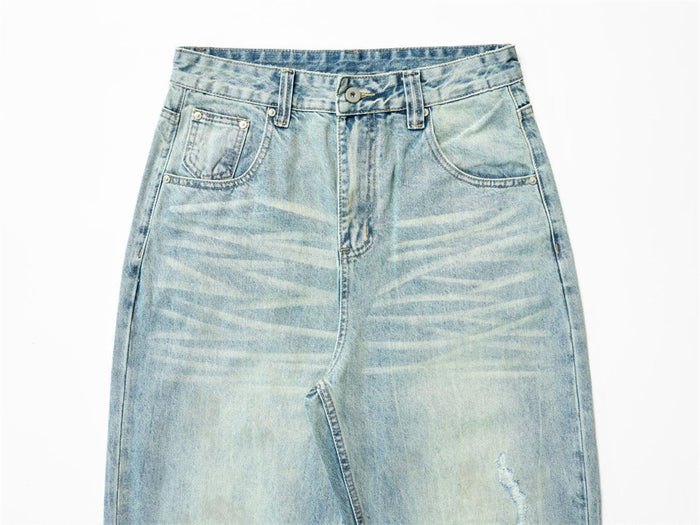 Close front view of light-wash denim jeans showing waistband, pockets, fly and faded whiskering
