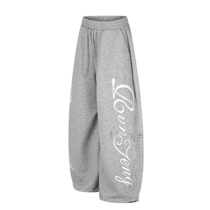 Gray wide leg sweatpants angled front view with white script graphic and rhinestone cross detail