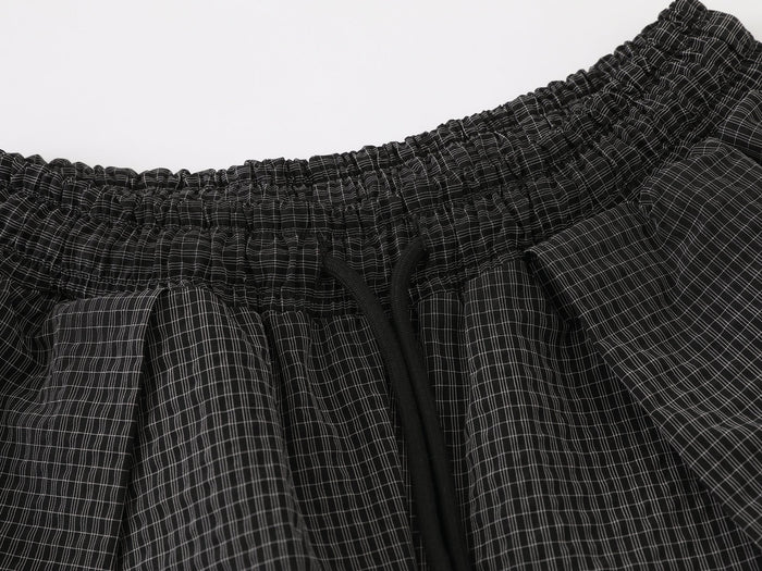 Close-up of black check pants waistband with elastic gathers and black drawstring detail