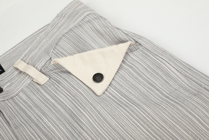 Close-up of a triangular cream front pocket flap with a dark round button on striped jeans