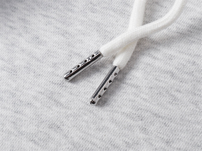 Close-up of white sweatpants drawstring ends with shiny perforated metal aglets on gray fabric