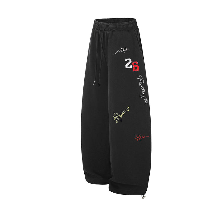 Angled front view of black wide-leg sweatpants showing the number 26, graffiti graphics, and cinched ankle hems