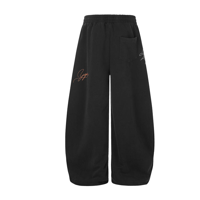 Back view of black wide-leg sweatpants with a rear pocket and small orange graffiti embroidery