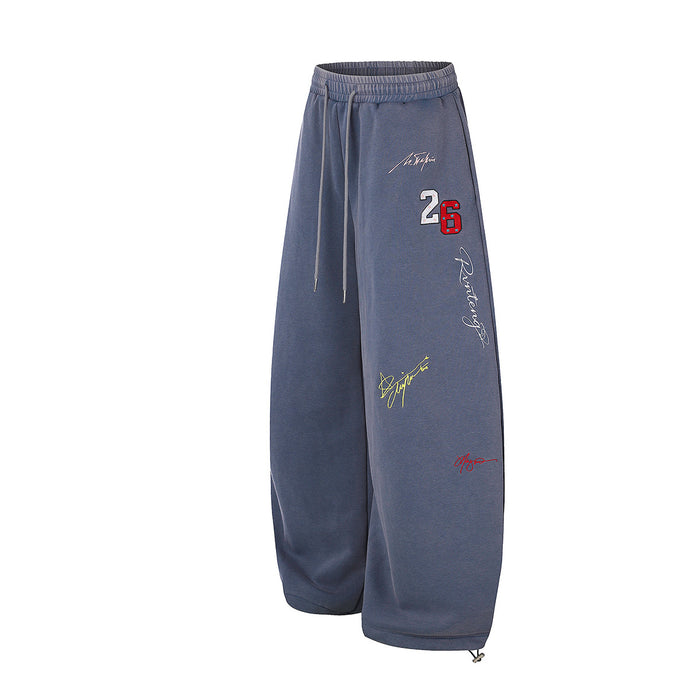 Angled front view of blue wide-leg sweatpants showing the number 26 and multicolor graffiti embroidery
