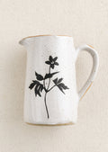 A small speckled white ceramic creamer pitcher with black flower silhouette.